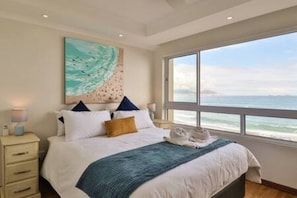 Una camera da letto con un letto, un comodino, un quadro e vista sull'oceano.