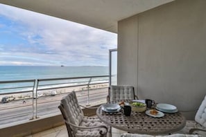 Un balcone con vista sulla spiaggia, un tavolo rotondo con piatti e una ciotola, e due sedie.