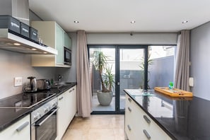 A modern kitchen with a stove, oven, and microwave, a glass-top island, and a potted plant.