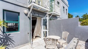 Un edificio moderno con balcón, una puerta que da a un espacio interior, y mobiliario exterior con sillas y una mesa.
