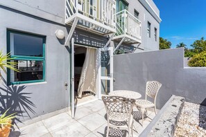 Un edificio moderno con un balcone, una porta che dà su un ambiente interno e un’area esterna con sedie e un tavolo.