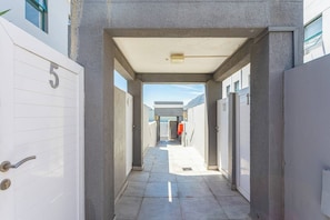 A corridor with doors numbered 5 and 11, leading to a covered area with a view of the sea.