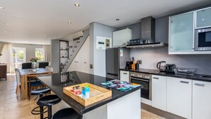 Una cocina moderna con una isla central, taburetes de bar, un comedor y una escalera que lleva a otro nivel.