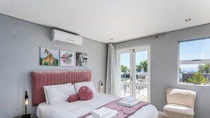 Un dormitorio moderno con una cama, una silla, obras de arte y una ventana.
