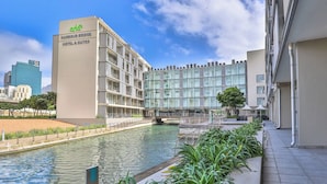 Un hotel moderno con fachada de vidrio, vista al agua y un puente que lo conecta con otro edificio.