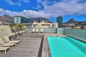Area piscina sul tetto con poltrona prendisole e vista su edifici e montagne.