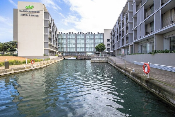 A modern hotel with a glass facade, located beside a canal with a bridge.