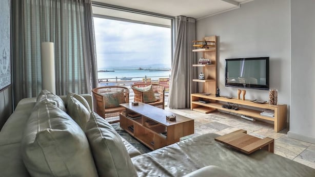 Una sala de estar moderna con sofá, mesa de centro, televisor y vista al mar.