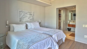 Habitación de hotel con cama, un mapa en la pared, baño con espejo y una puerta que da a otra habitación.