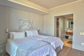 Una camera d'albergo con un letto, una mappa appesa al muro, un bagno con uno specchio e una porta che conduce a un'altra stanza.