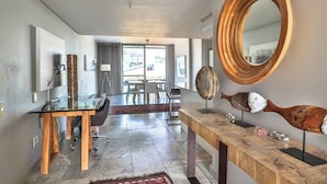 Habitación de hotel moderna con un escritorio de vidrio, una zona de comedor con vistas y una escultura original de madera con forma de pez.