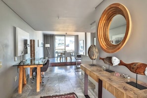 Una moderna camera d'hotel con una scrivania in vetro, un'area ristorazione con vista e una scultura di pesce in legno originale.