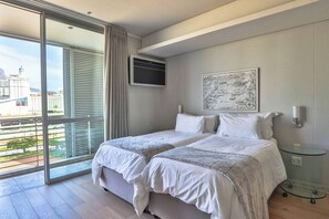A hotel room with a balcony, a bed with white bedding, a mounted flat-screen TV, and a cityscape view.