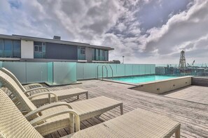 A rooftop pool area with lounge chairs and a view of the sea and industrial structures.