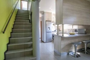 Una cocina moderna con una isla central, electrodomésticos de acero inoxidable y una escalera con una pared verde.