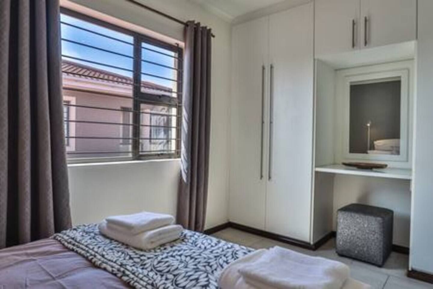 Habitación de hotel con cama, armario, taburete pequeño y ventana con cortinas.