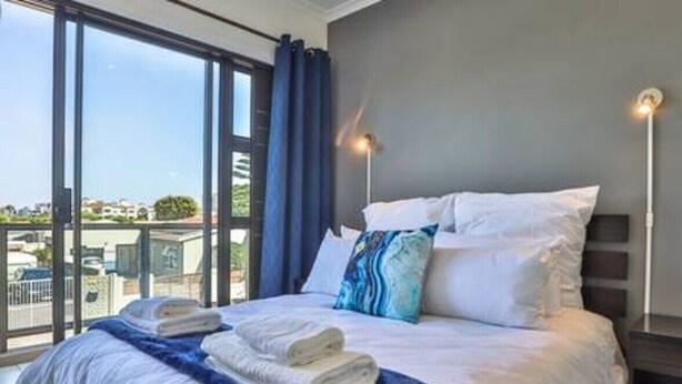 A hotel room with a large bed, a view through the window, and a nightstand with a lamp. - Modern 3 Bedroom with spacious braai area by Ctha (Century City)