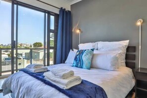 Una camera d'albergo con un letto grande, vista attraverso una porta vetrata e un comodino con una lampada.