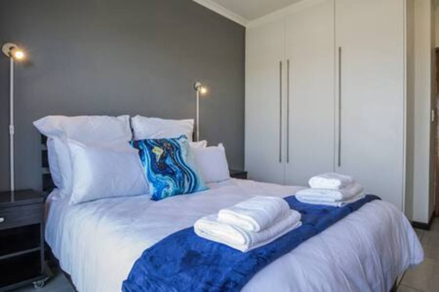Une chambre d’hôtel avec un lit, des oreillers, une couverture bleue et une armoire.