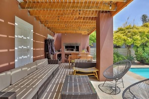 Un'area salotto esterna coperta con barbecue, piscina e struttura a soffitto in legno.