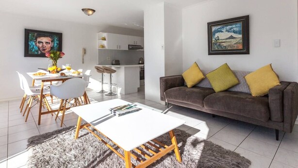 Un salon moderne avec un canapé, une table à manger et des chaises, et un coin cuisine à l’arrière-plan.