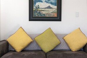 A room with a sofa against a wall, a framed painting above it, and a light switch to the right.