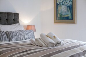 A neatly made bed with striped bedding, a headboard, and a lamp in the background.