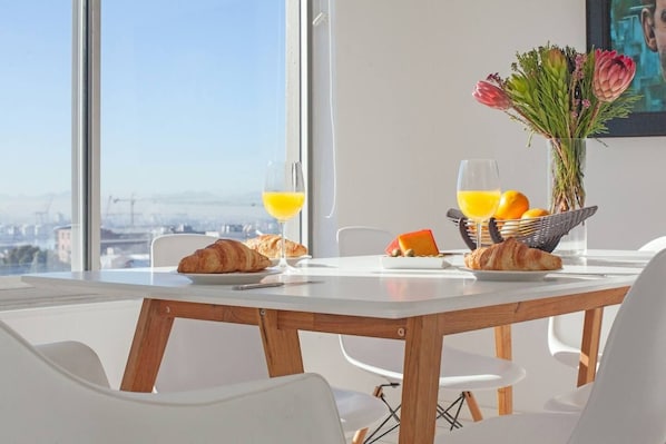 A breakfast setting with croissants, orange juice, and a fruit bowl on a table with a city view.