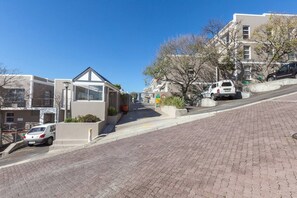 A residential street with houses, a paved road, and parked vehicles.