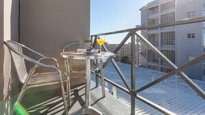 Un balcon avec une table, des chaises et un verre de jus d’orange.