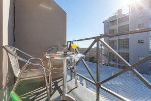 Un balcone con tavolo, sedie e un bicchiere di succo d'arancia.
