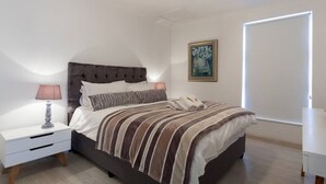 Une chambre à coucher avec un lit, des tables de chevet, une lampe, un tableau et une porte.