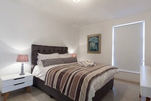 Una camera da letto con un letto, comodini, una lampada, un quadro e una porta.