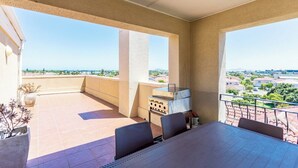 Un balcone con tavolo e sedie, un barbecue e vista su una zona residenziale.