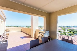 Un balcón con mesa y sillas, una parrilla y vistas a una zona residencial.