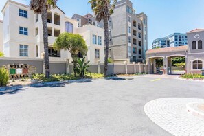 Un edificio residencial de varios pisos con un área de entrada pavimentada, palmeras y un cartel que dice 'Villa Italia'.