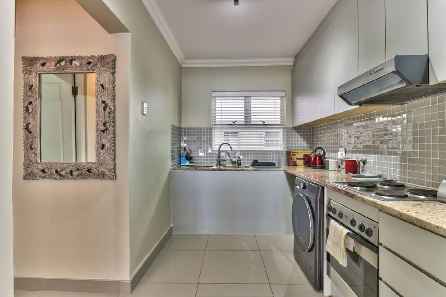 A modern kitchen with a built-in oven, a washing machine, and a window with blinds.