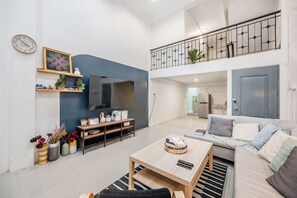 Ein modernes Wohnzimmer mit Fernseher, Sofa, Couchtisch und einem Balkon.