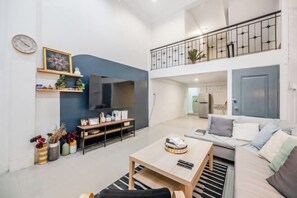 Ein modernes Wohnzimmer mit einer Couch, einem Couchtisch und einem Fernseher. Es gibt einen Balkon mit Geländer und einer Tür.