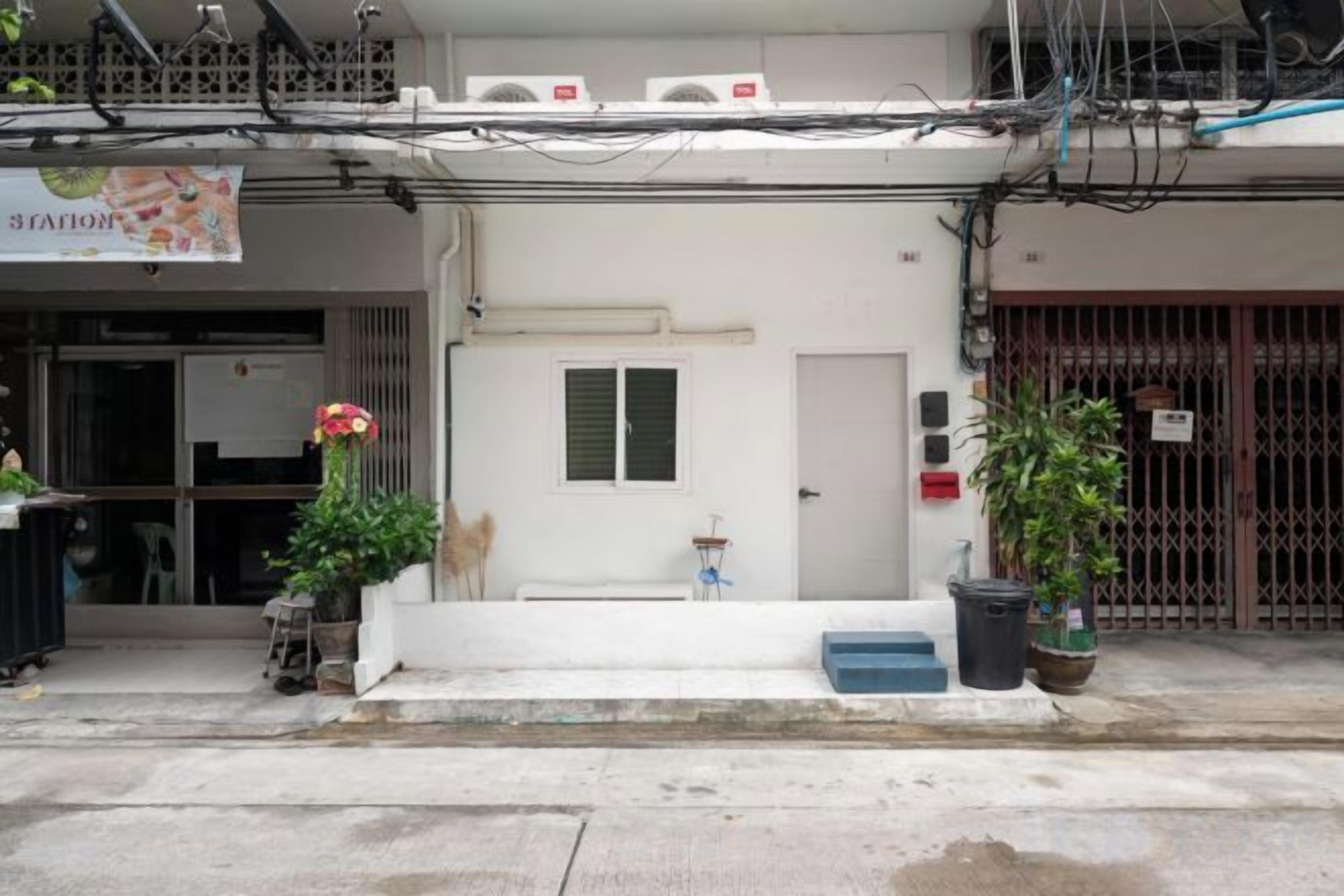 A building with a white facade, a door with a window, and a small step leading to the entrance. There are potted plants on the sidewalk.