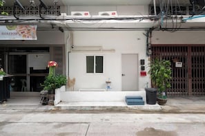 A building with a white facade, a door with a window, and a small step leading to the entrance. There are potted plants on the sidewalk. - Bangkok Group Haven - 6BR Bangchak BTS 12 sleeps (Bangkok)