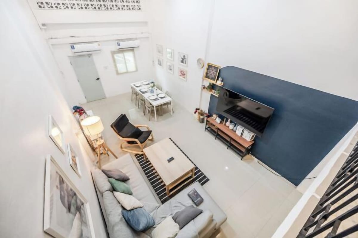 A spacious living area with a sofa, coffee table, and a dining table set up. There is a staircase on the right and a door leading to another room.