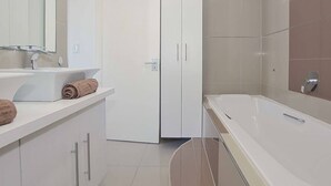 A modern bathroom with a white sink, a towel, a white wardrobe, and a bathtub. - 3br Beach Stay | Views & backup power by ctha (Cape Town)