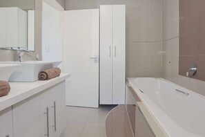 Un bagno moderno con un lavandino bianco, un asciugamano, un armadio bianco e una vasca da bagno.