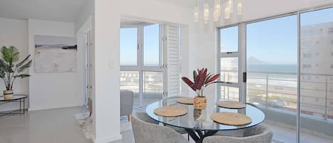 A modern dining area with a glass table, four chairs, and a view of the city through large windows.