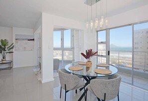 Un'area pranzo moderna con un tavolo in vetro, quattro sedie e vista sulla città attraverso ampie finestre.