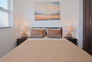 Una camera da letto con un letto grande, due comodini con lampade, un quadro sopra il letto e una finestra con persiane.