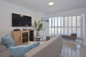 A modern living room with a flat-screen TV, a wooden cabinet, a round table with a plant, and two sofas.