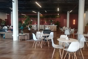 A spacious indoor area with multiple seating arrangements, including tables and chairs, and a reception desk in the background.