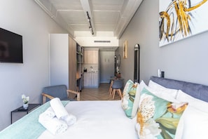 A modern hotel room with a bed, a desk, and a kitchenette.
